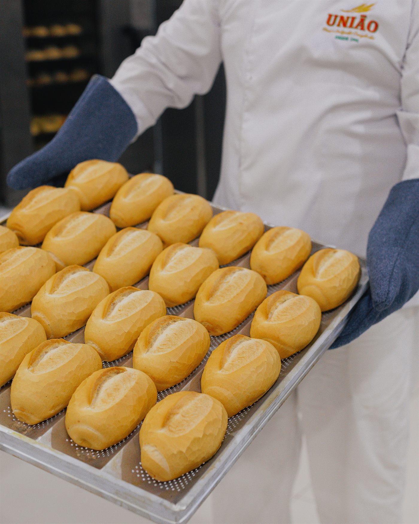 Padeiro da União segurando bandeja de pães franceses assados